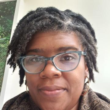 A black woman facing the camera, wearing glasses, with short black hair and a slight smile.