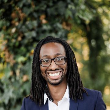 A young man facing the camera smiling wide and wearing glasses.